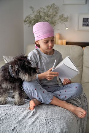 Boy in pink scarf opening notebook near dog