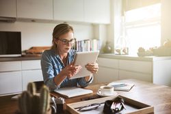 Woman holding and reading tablet at kitchen table