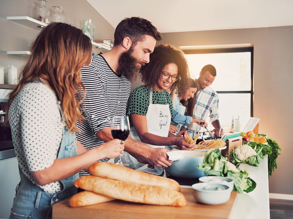 Friends in a bright kitchen cooking pasta and vegetables