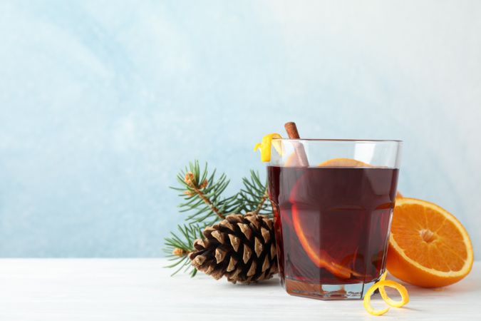 Glass of tasty mulled wine with orange on blue wooden background, space for text