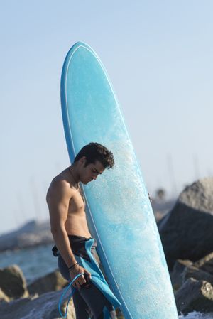 Male surfer with blue board standing in the water around a rocky beach