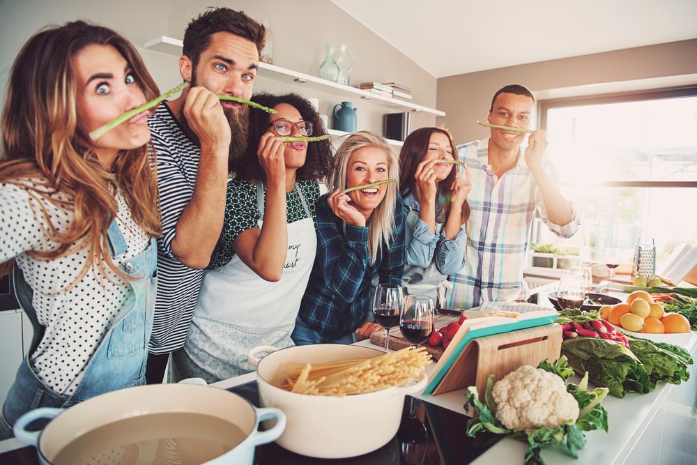 Friends making funny faces with asparagus mustaches in the kitchen