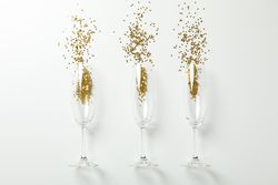 Champagne glasses with glitter on light background, space for text