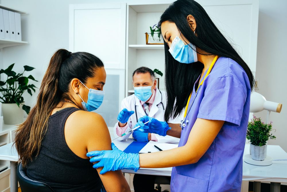 Medical assistant vaccinating female patient in doctor’s office