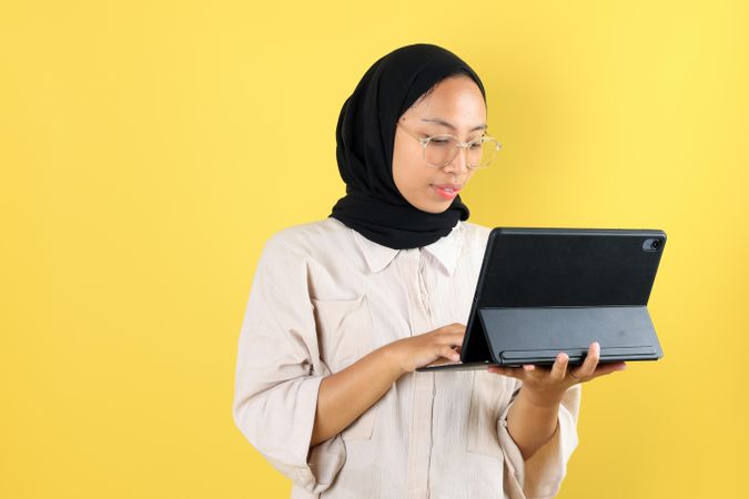 Portrait of Smiling Young Asian Muslim Woman Wearing Hijab Holding Digital Tablet, Looking at Tab.