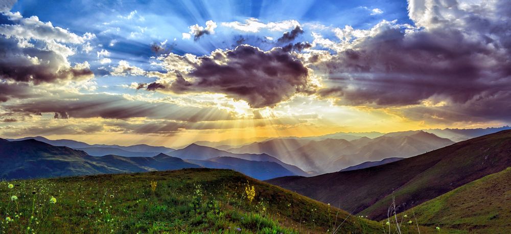 Sunlight explosion behind dark clouds over green hills