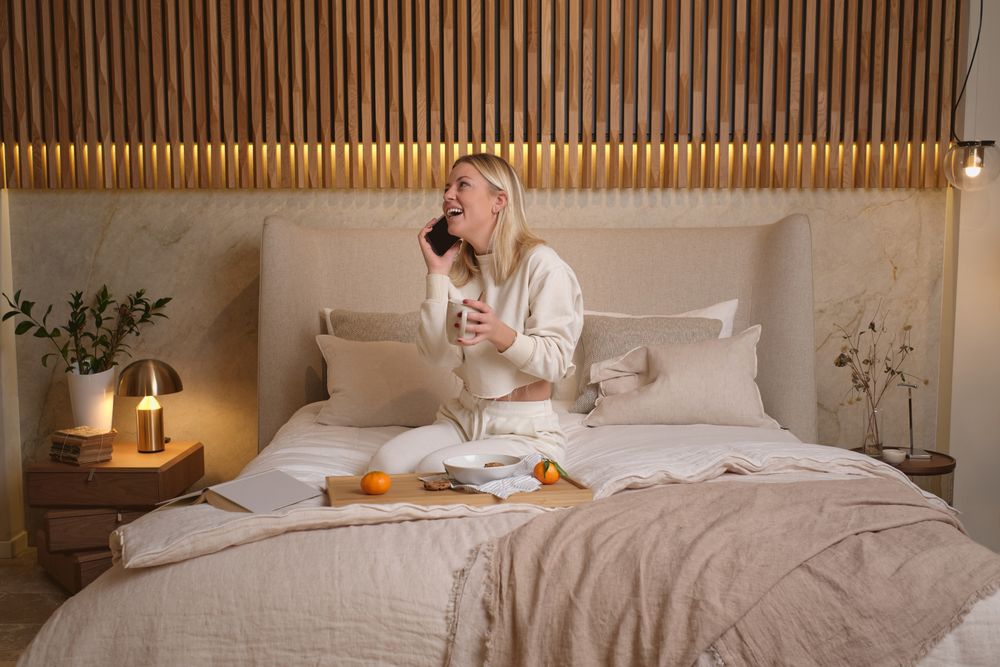 Young female with smartphone eating in bed