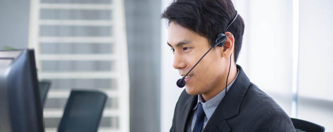Side view of Asian man working at service desk talking on phone