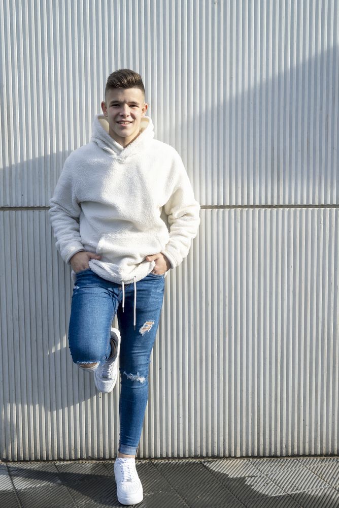 Portrait of young man with hands in pocket leaning on wall outside