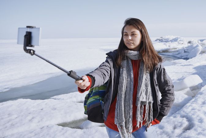 Female traveler outdoors at icy landscape using selfie stick
