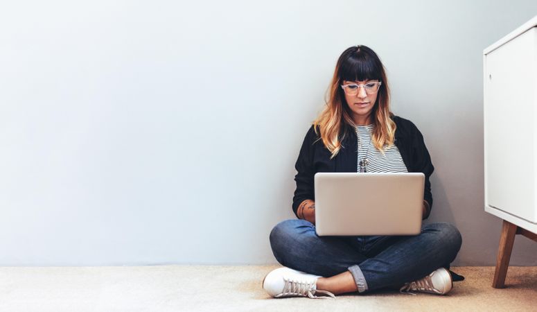 Female freelancer working on laptop sitting on floor