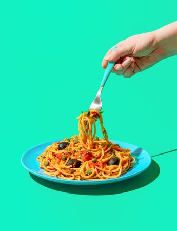 Eating spaghetti puttanesca, a vegan pasta dish, minimalist on a green background