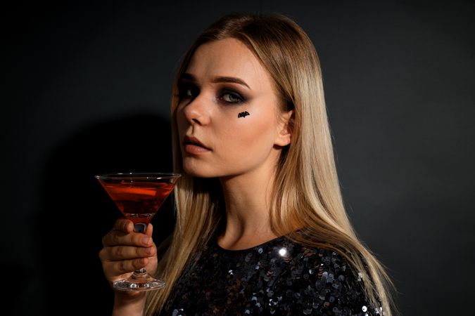 A woman at a party in the style of Halloween with a cocktail in her hands