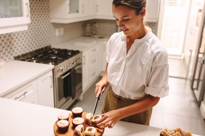 Woman standing in kitchen and slicing cupcake open