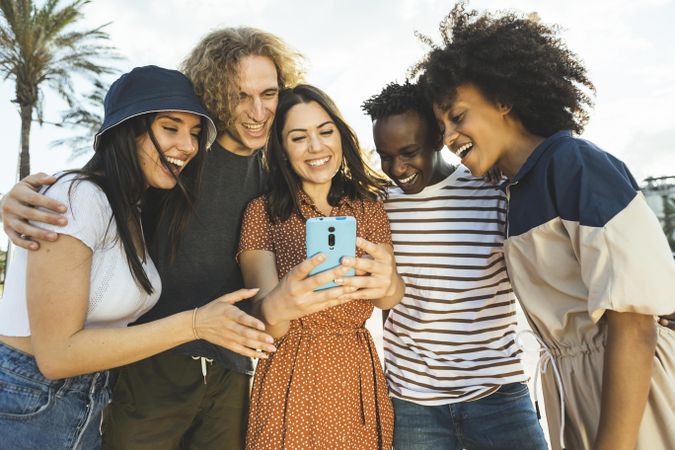 Multiracial group of young adults looking at smartphone while walking in the street