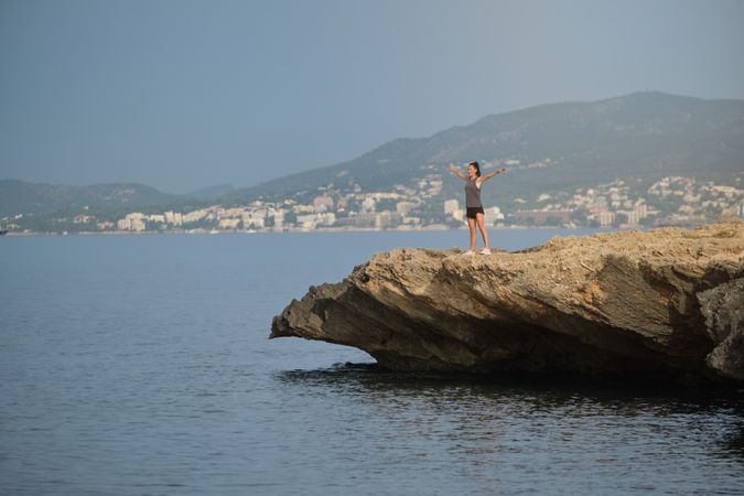 Young woman standing on stone cliff with spread arms