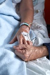 Crop faceless man with sick wife holding hands in hospital