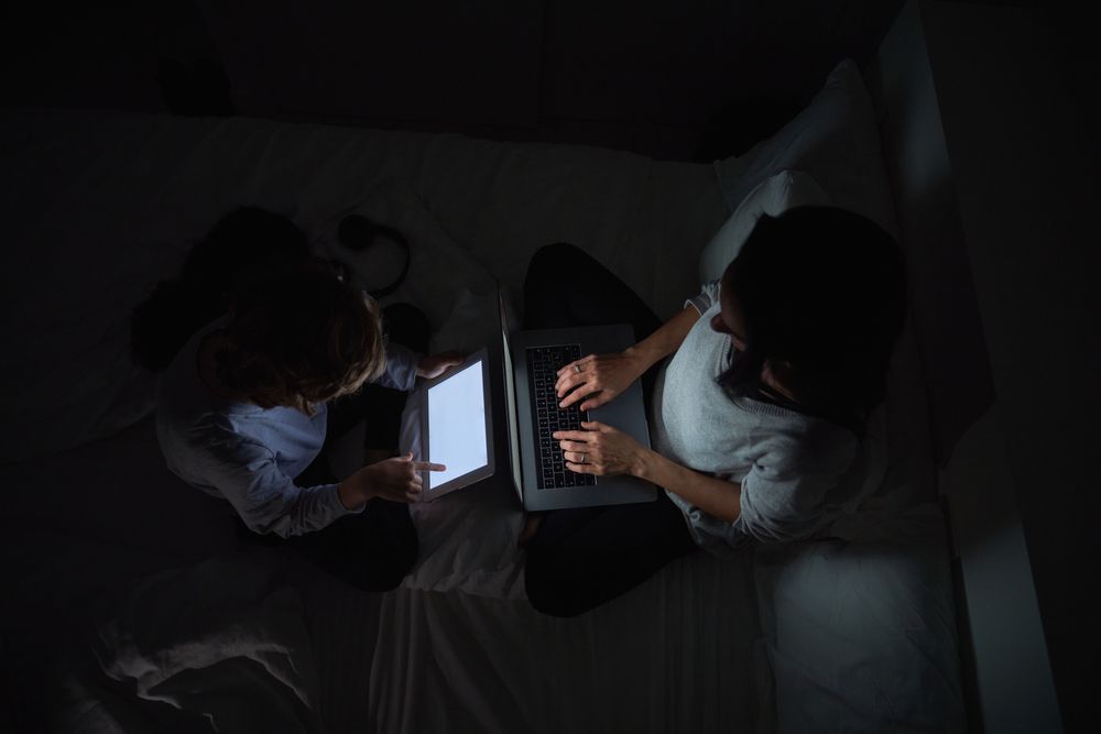 Mother with son browsing gadgets while doing homework in darknes