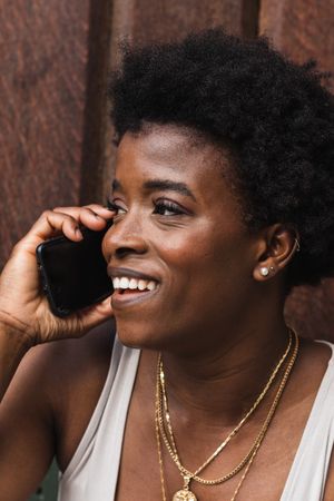 Smiling Black woman talking on smartphone sitting near building
