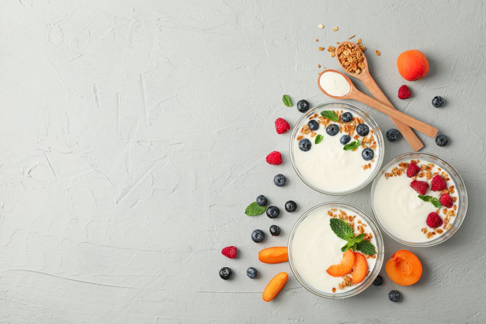 Flat lay composition with yogurt desserts and fruits on grey cement background