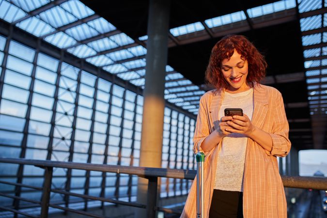 Smiling young woman browsing phone at station