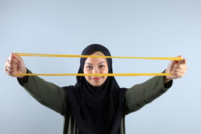 Young Asian Hijab Woman Stretch Yellow Resistance Band for Hand Pilates Exercise
