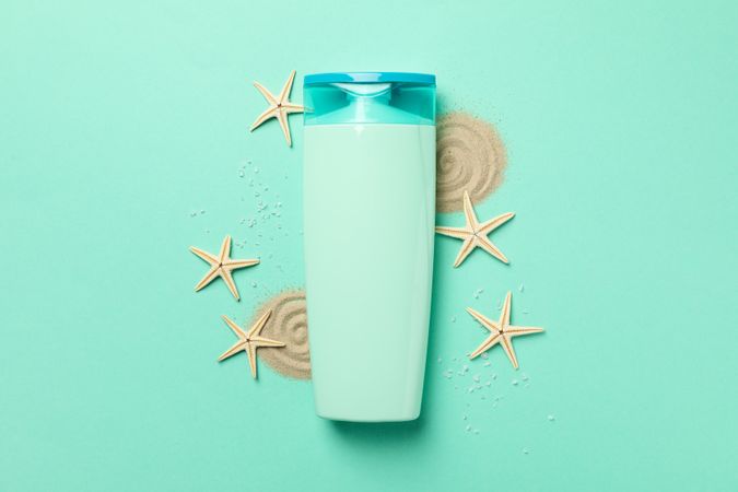 Bottle of shampoo, starfishes and sand on mint background