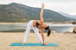 Woman practicing yoga outdoors near water