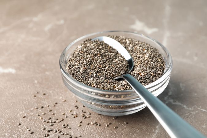 Glass sauce boat with chia and spoon on textured background, close up
