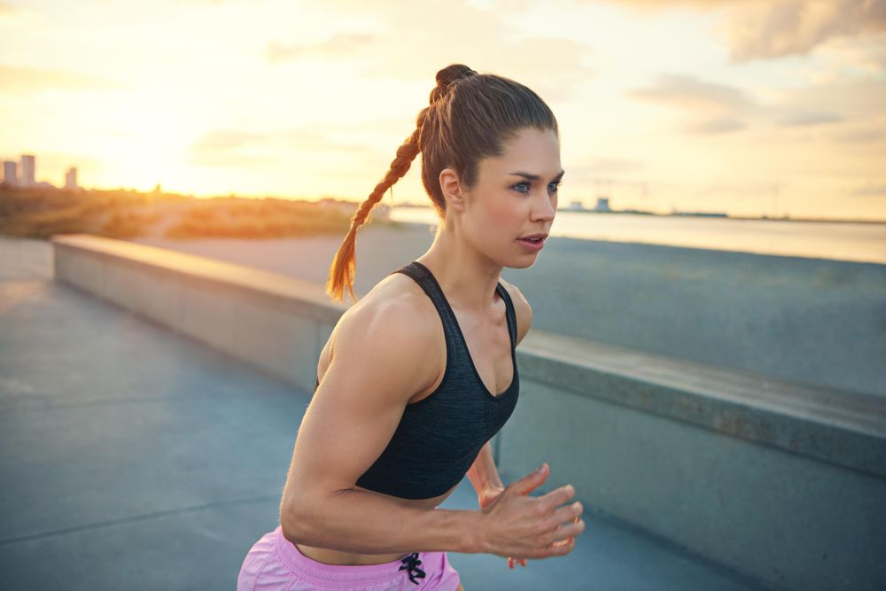 Focused woman with high pony tail running outside