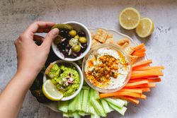 Person dipping carrot stick into hummus decorated with vegetables