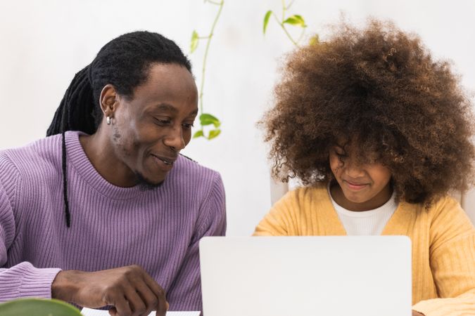 Black father helping daughter with homework on laptop