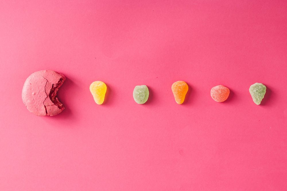 Pacman French macaron approaching line of gummies on pink background