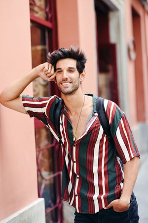 Man with dark hair wearing casual clothes leaning on wall outdoors