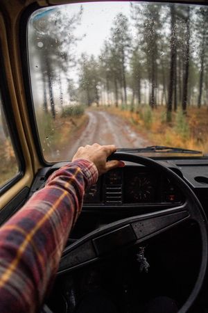 Driver riding car along rural pathway at forest in rain