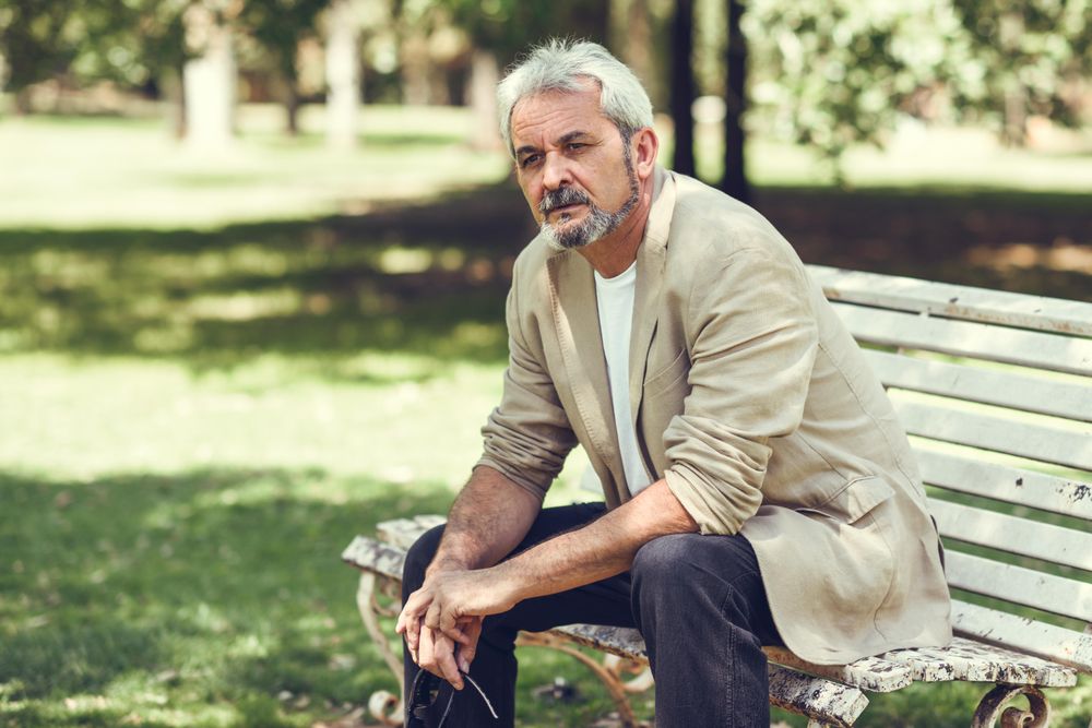 Portrait of a mature man, sitting forward on bench in a park with copy space