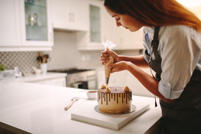 Female wearing apron decorating chocolate cake in kitchen