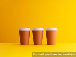 Three disposable coffee cups on yellow background 42Ld10