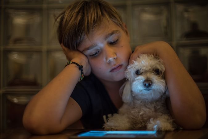 Boy looking at tablet screen while hugging a dog