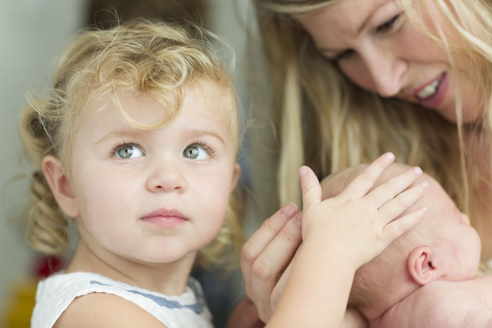 New Mom Holds Newborn Baby Girl as Young Sister Looks