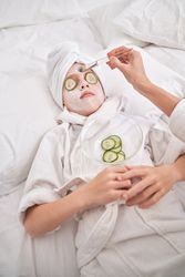 Unrecognizable mother applying mask on face of child during spa