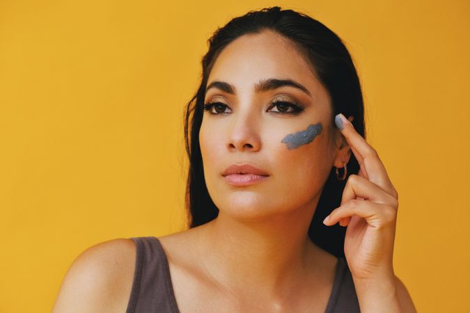 Latina woman looking away while applying clay mask with hand