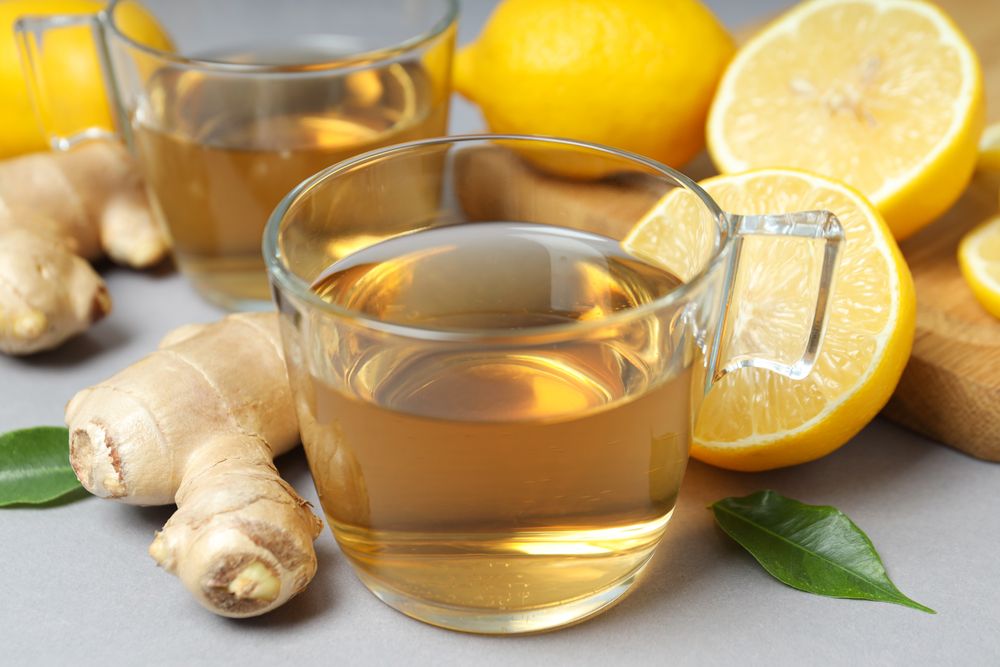 Cups of tea, ginger and lemons on gray background, close up