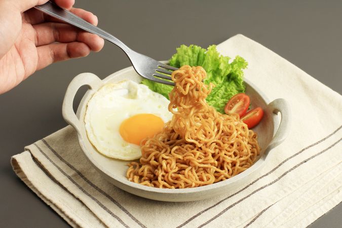 Person's fork lifting noodles from indomie goreng, Indonesian noodles and egg dish