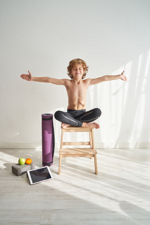 Preteen boy sitting in Padmasana with arms apart on stool