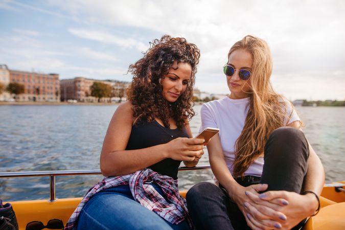 Two women friends looking at photos on mobile phone while on a boat