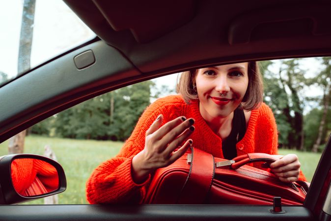 Woman putting suitcase in front window of car