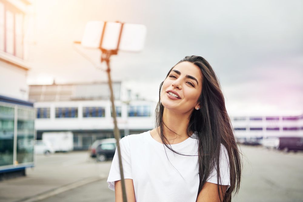 Woman posing with selfie stick in parking lot on overcast day