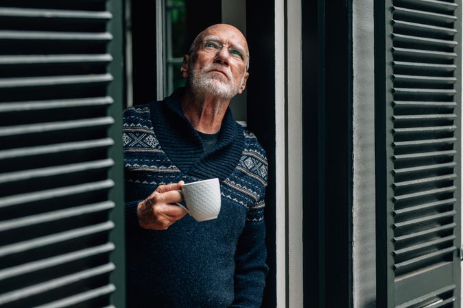 Man looking up standing at the window with a coffee cup in hand