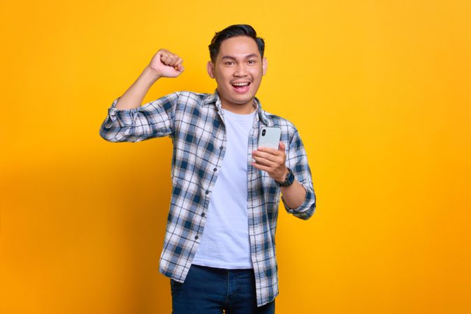 Very happy Asian male holding his phone with his fist raised in celebration